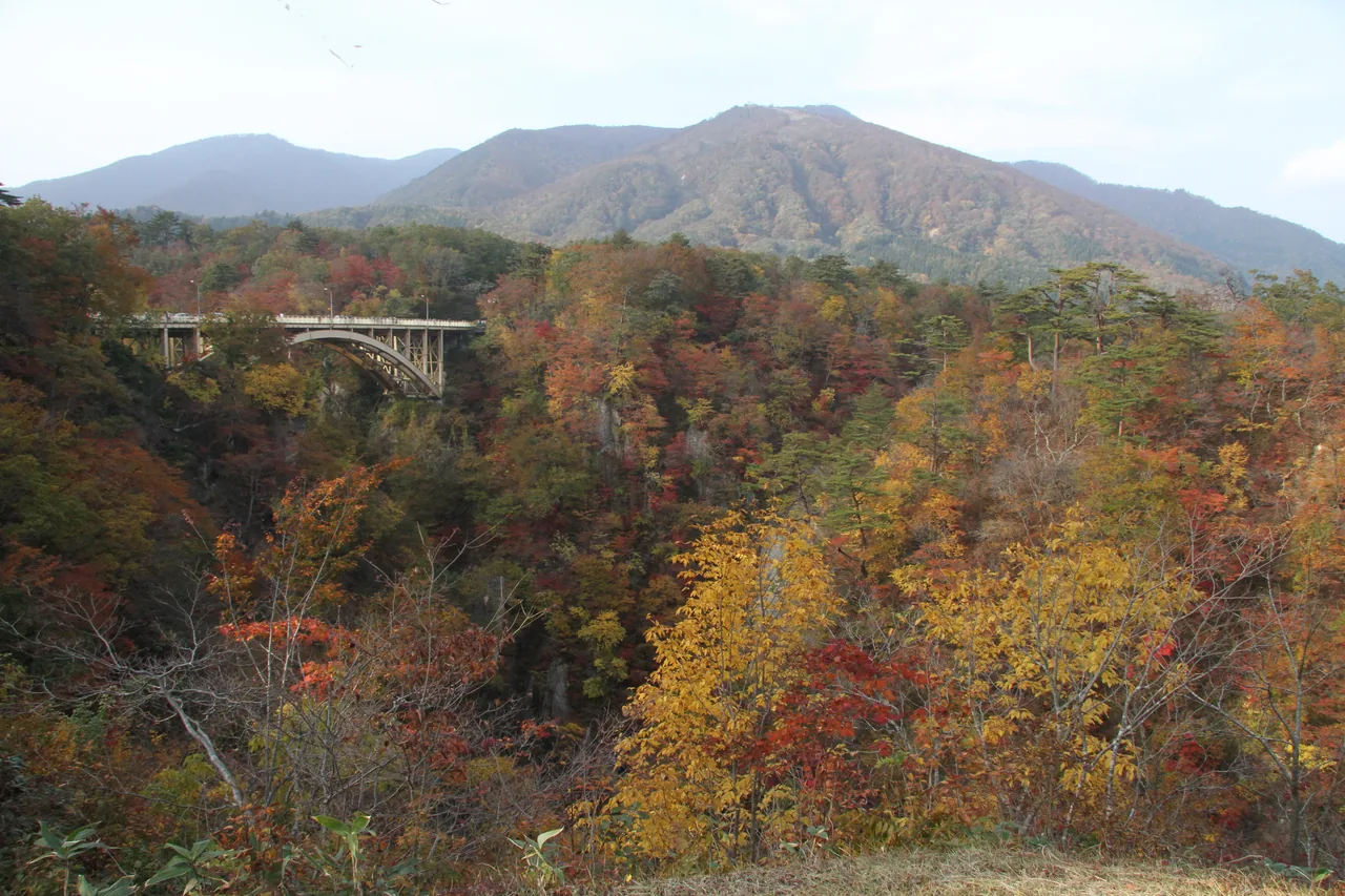 A red and gold maple gorge in northern Japan in October, with autumn-colored trees lining a rocky river and steep cliffs under a clear sky