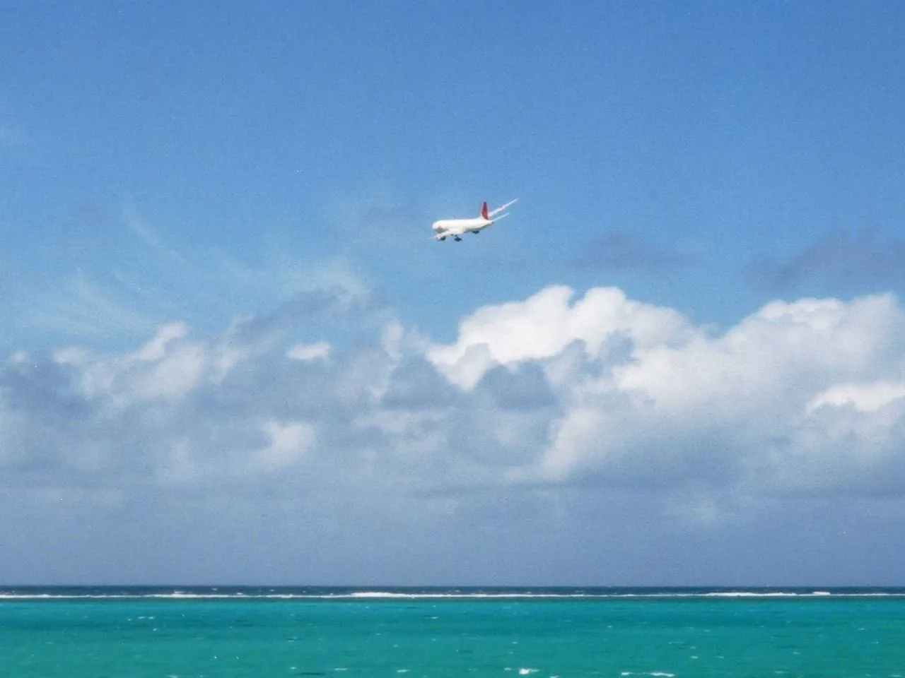 A plane drops low over a gradient of turquoise on its final approach to Shimojishima — the view from 17END.