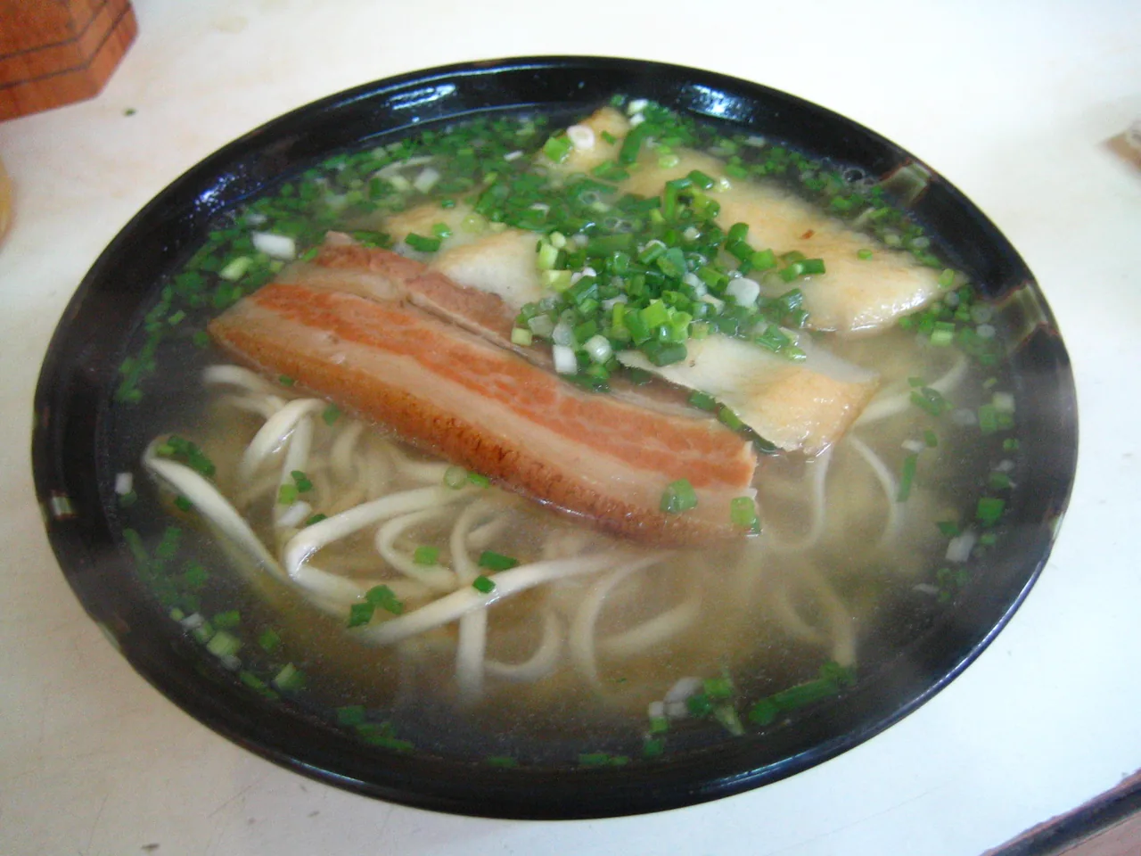 A bowl of Miyako soba — flat noodles in a clear, light pork-and-bonito broth, the pork belly traditionally tucked out of