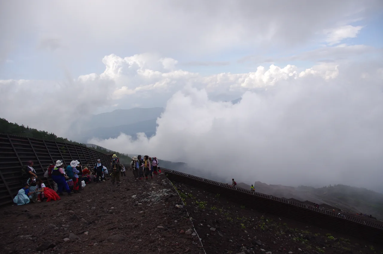 Hikers on Mount Fuji's upper trail strung out along the path above a vast sea of clouds at dawn