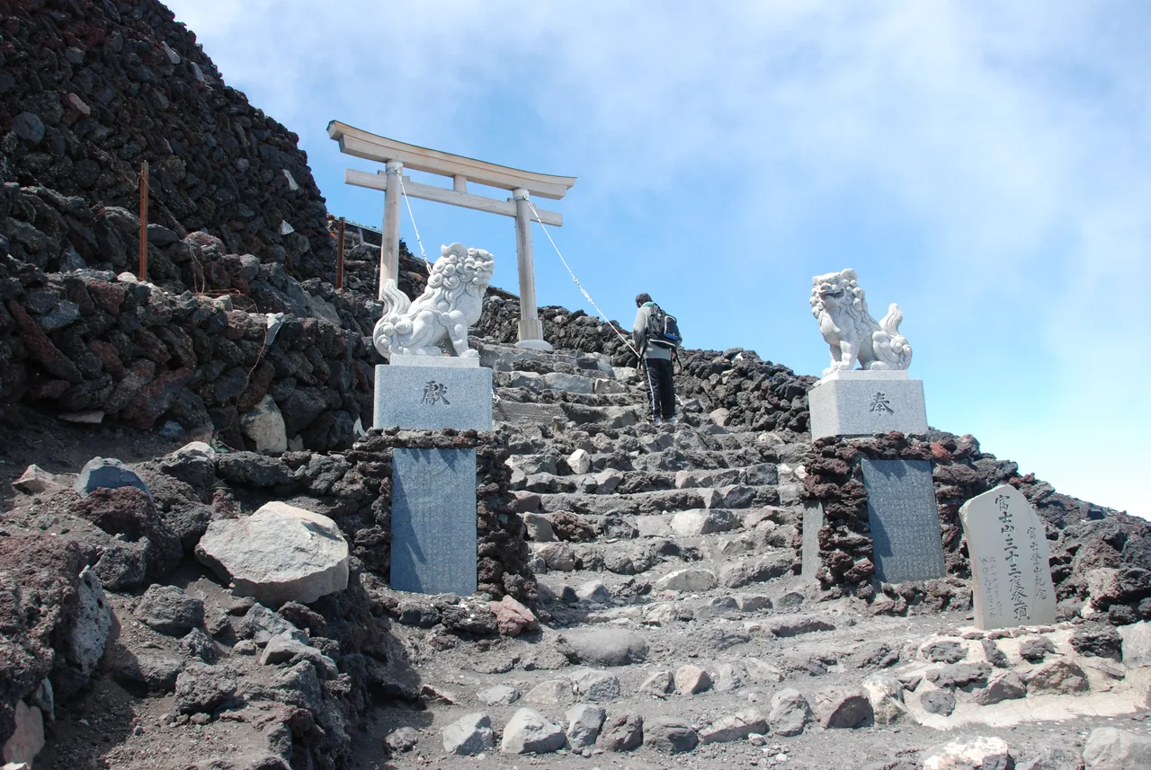 A weathered torii gate and stone komainu greet you at the summit shrine — proof you actually made it.