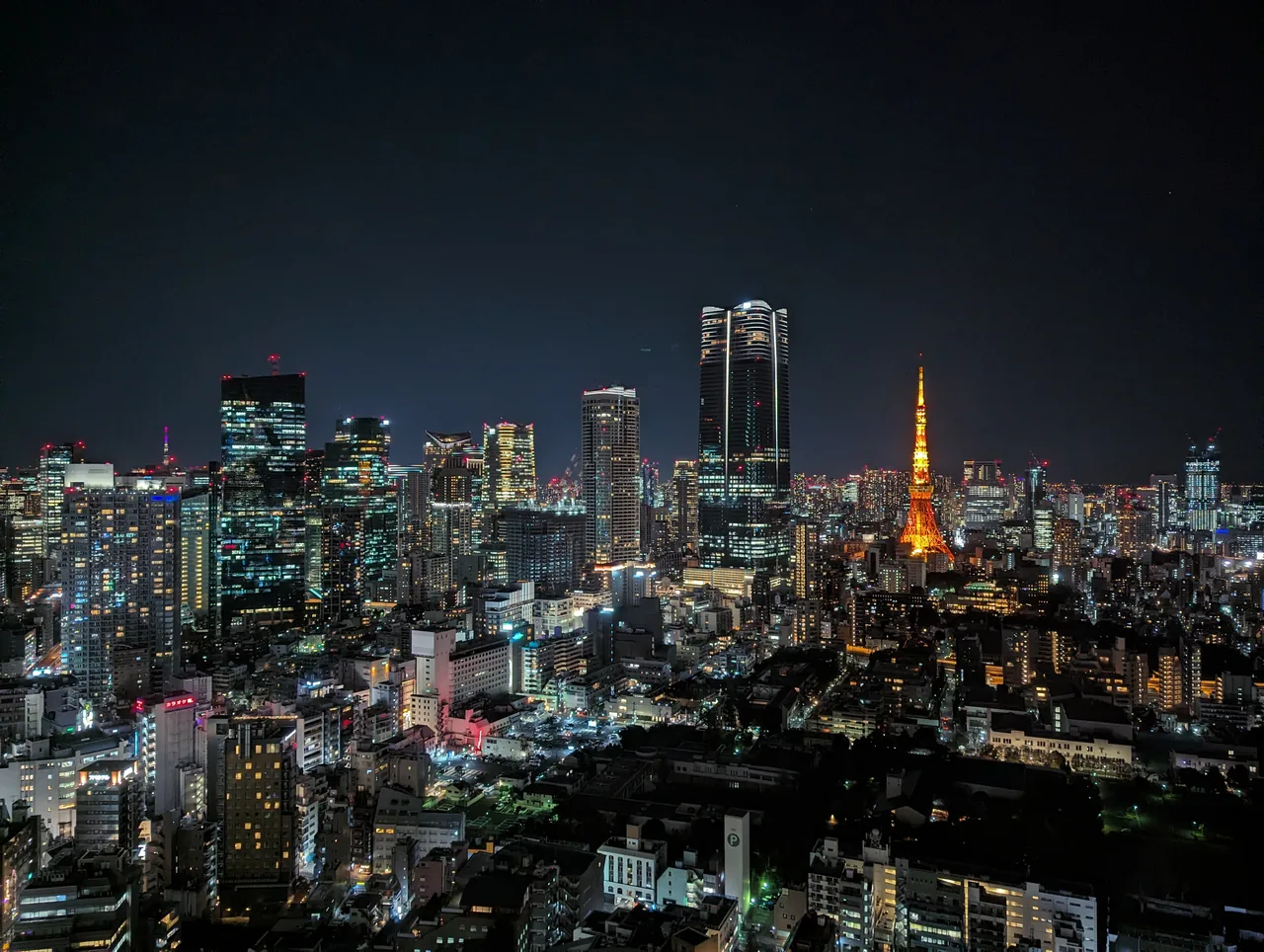 Azabudai Hills Mori JP Tower lit up at night beside Tokyo Tower