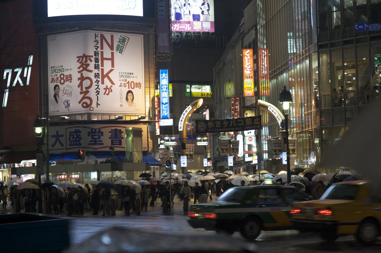 Crowds with umbrellas crossing Shibuya in the rain at night