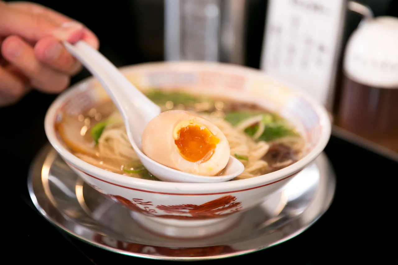 A bowl of Hakata tonkotsu ramen with a soft egg lifted on a spoon