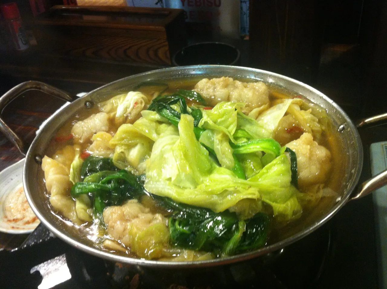 A metal pot of motsunabe piled with cabbage and garlic chives over offal in broth