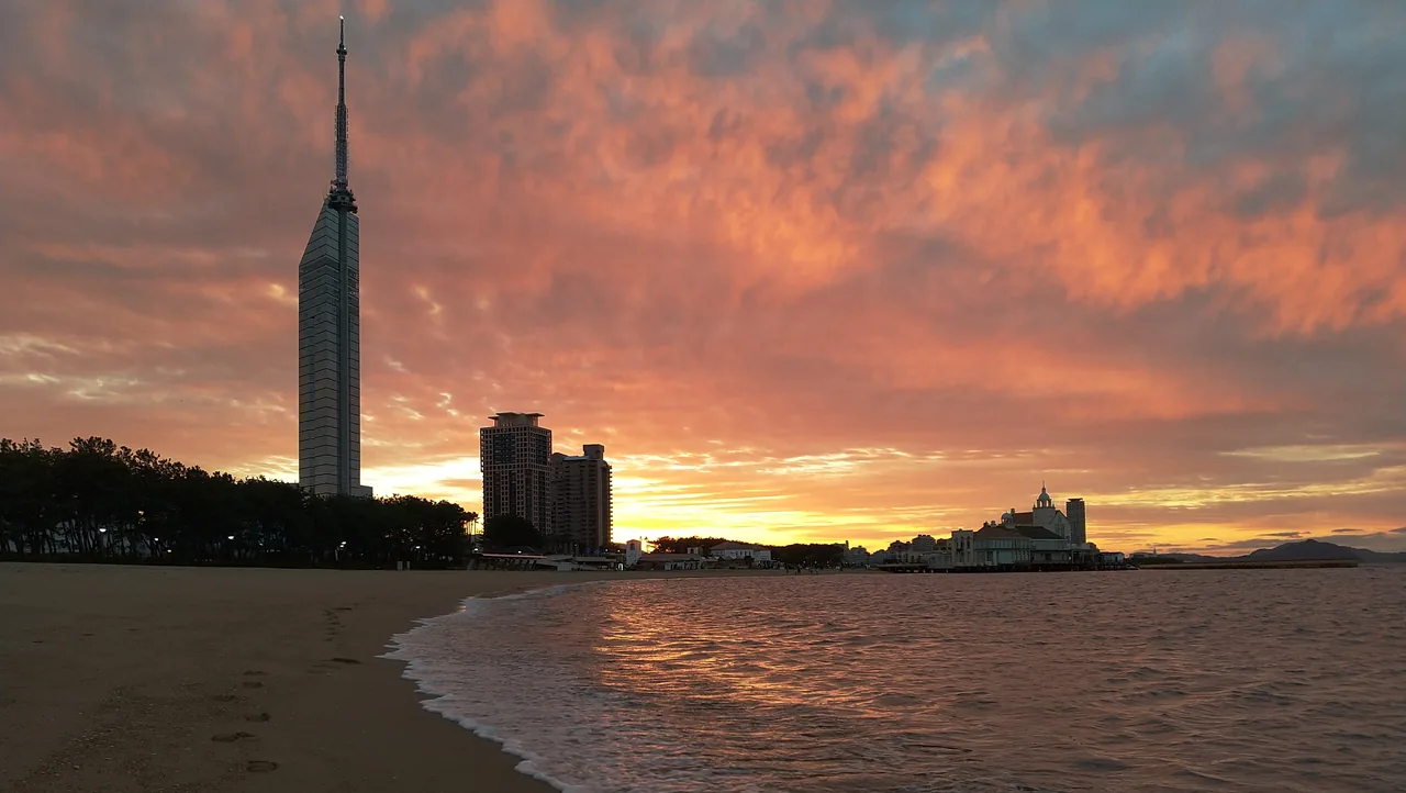Fukuoka Tower silhouetted against an orange sunset over Momochi Beach Fukuoka Tower silhouetted against an orange sunset over Momochi Beach