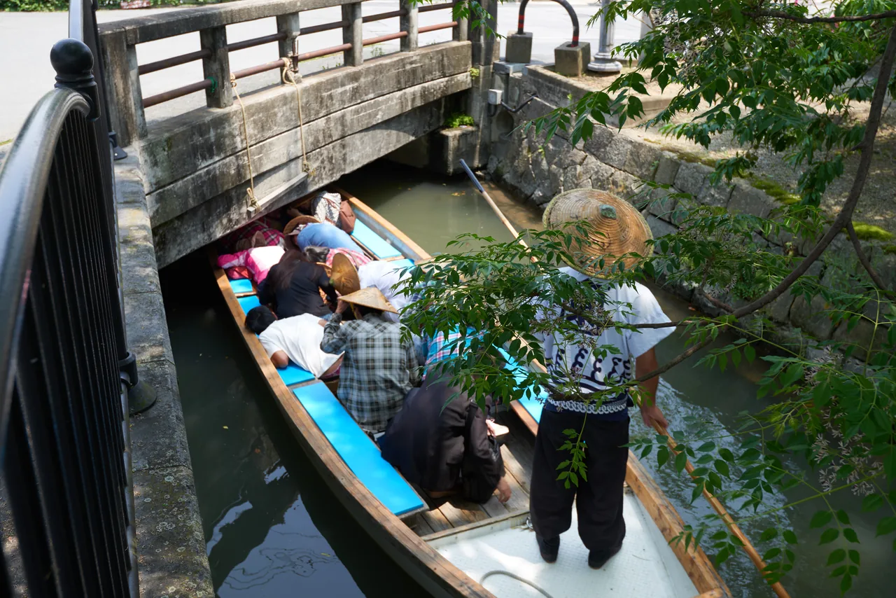 Passengers ducking under a low bridge on a Yanagawa canal boat, poled by a boatman in a straw hat Passengers ducking under a low bridge on a Yanagawa canal boat, poled by a boatman in a straw hat