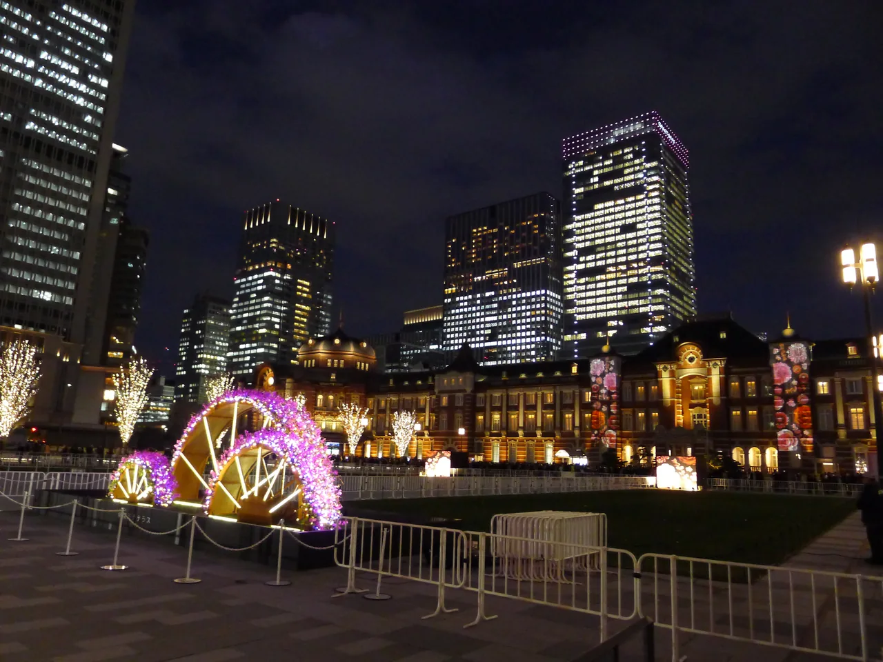 Illuminated trees and lights on the plaza in front of the Marunouchi facade of Tokyo Station after dark