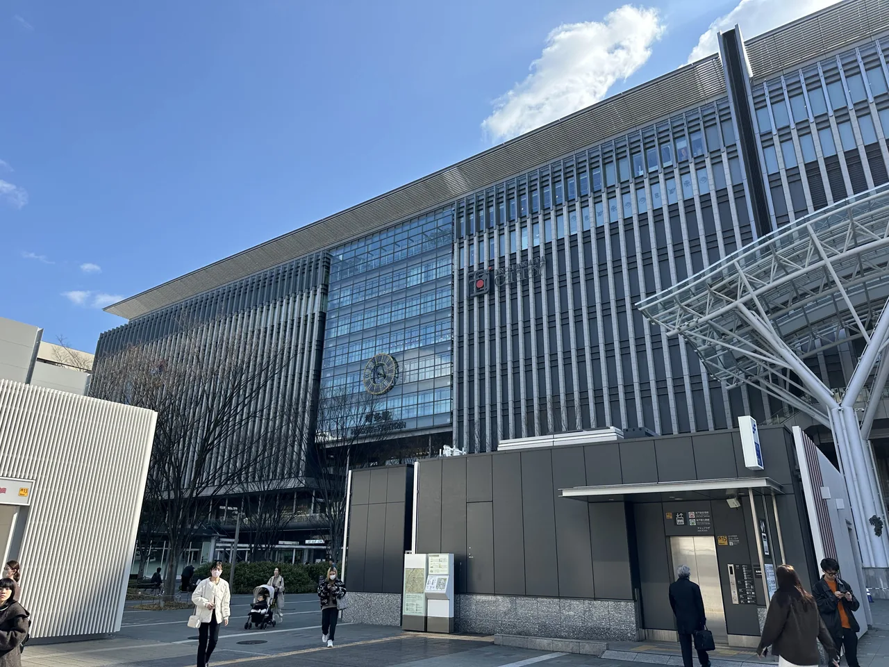 The JR Hakata City facade in Fukuoka, with its large clock, the station canopy and a subway entrance below, under a clear sky.