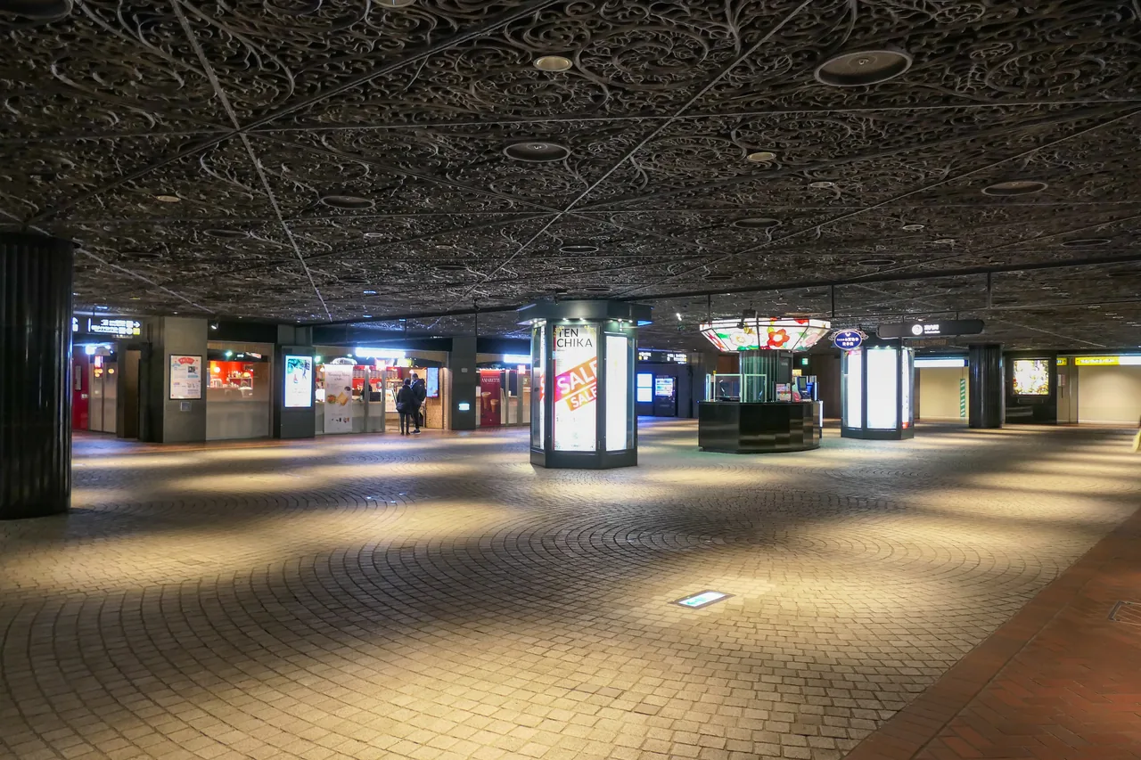 Tenjin Chikagai, the underground shopping arcade in Fukuoka, with its ornate patterned ceiling, warm lighting, stone paving and an information kiosk at the centre.