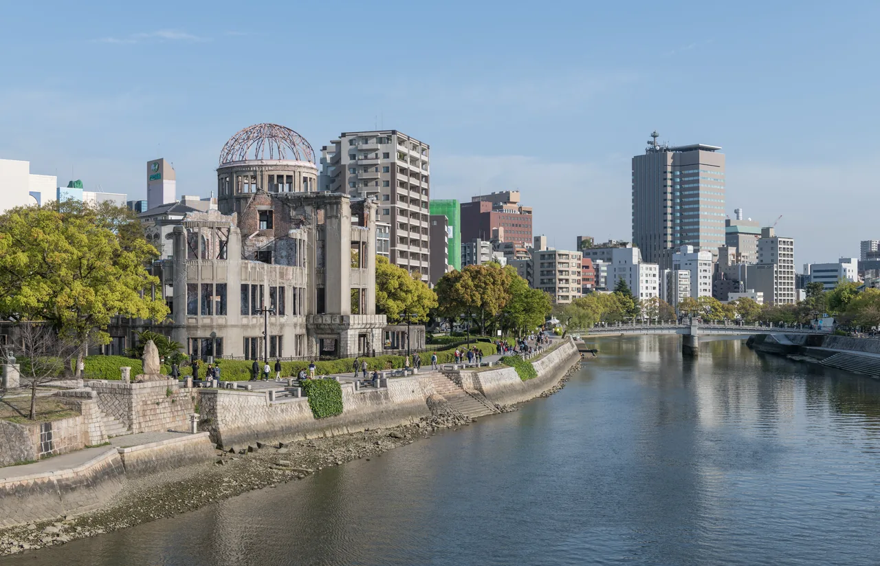 The A-Bomb Dome standing beside the Motoyasu River in central Hiroshima, with office towers and apartment blocks along the far bank