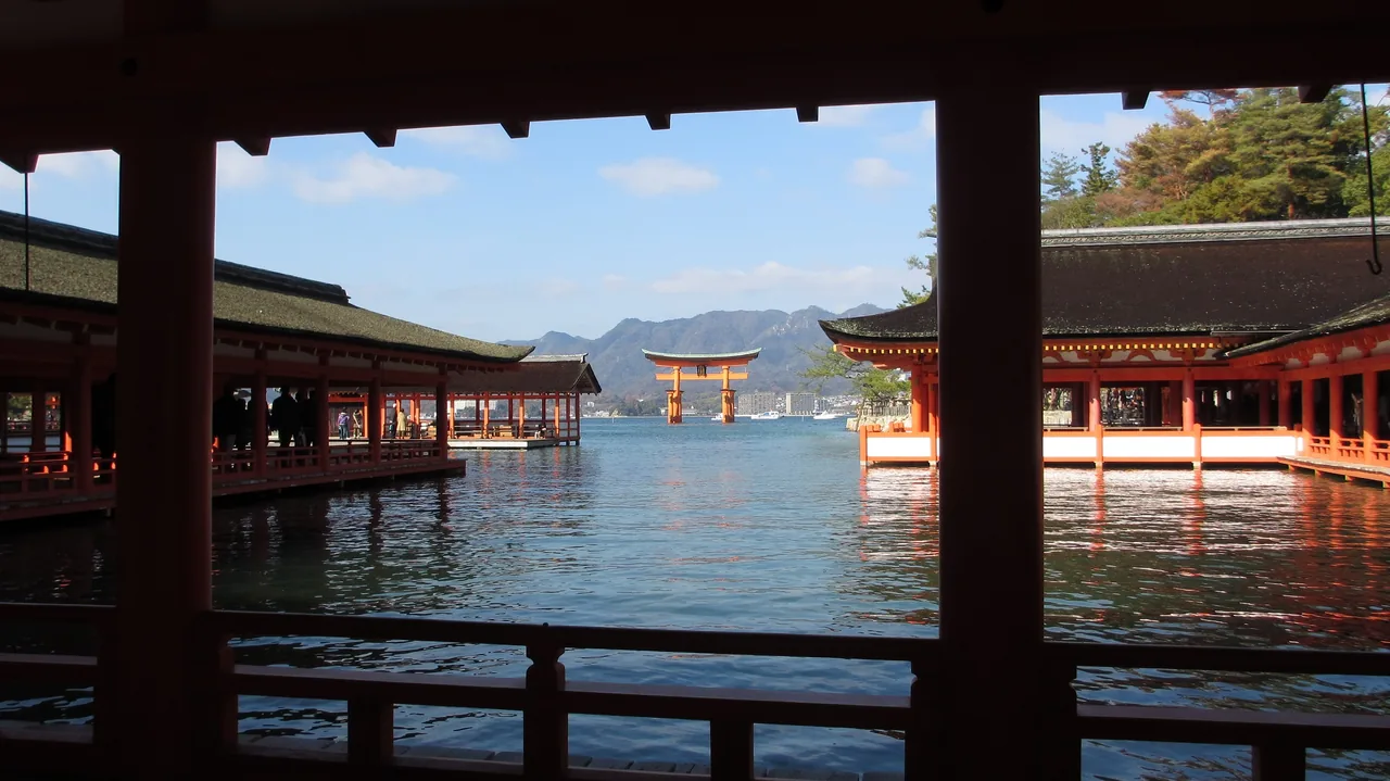 The great torii of Itsukushima Shrine seen from inside the shrine's vermilion corridor at high tide, with water beneath the walkways