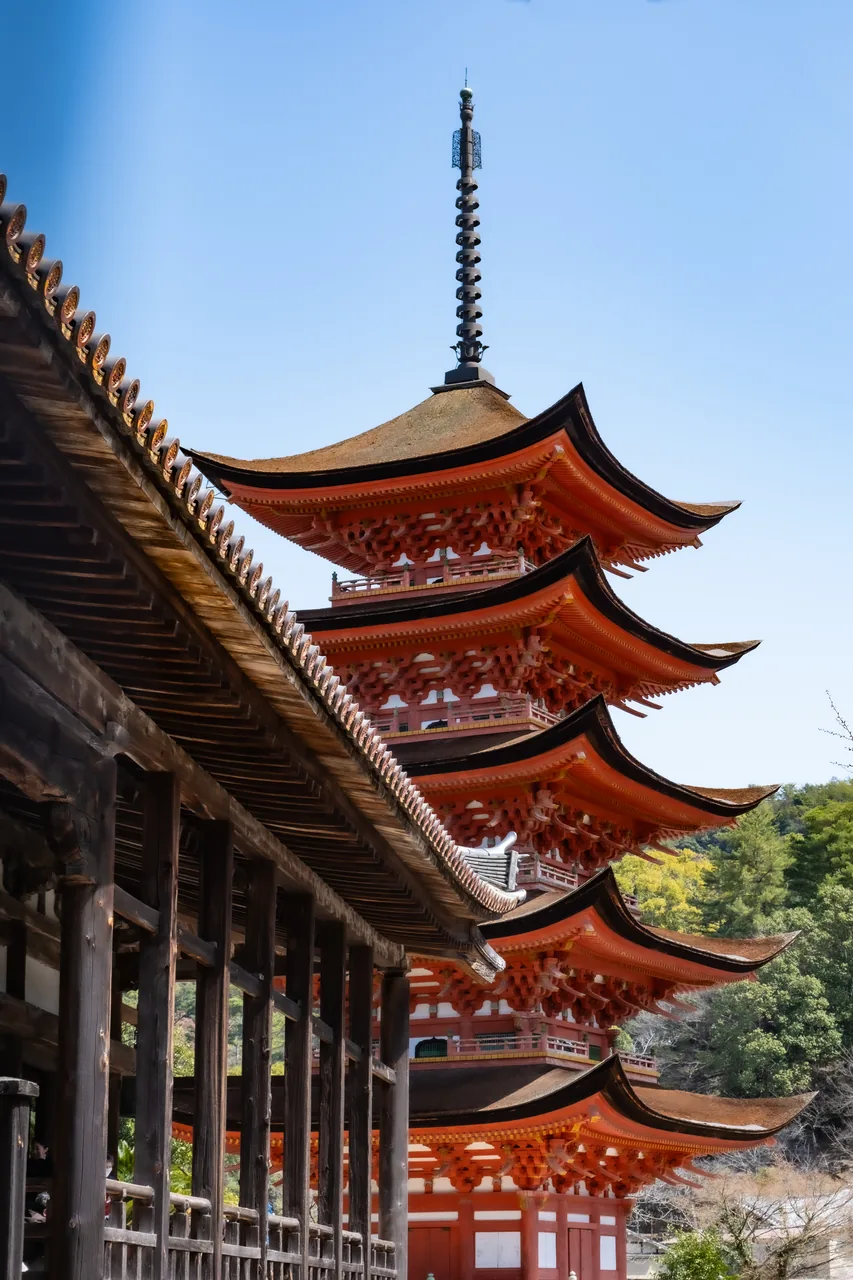 The vermilion five-storey pagoda on Miyajima rising behind the weathered timber columns and eaves of Senjokaku hall