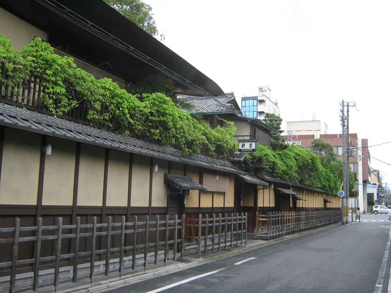 A row of traditional Kyoto ryokan behind a wooden lattice fence on a quiet street A row of traditional Kyoto ryokan behind a wooden lattice fence on a quiet street
