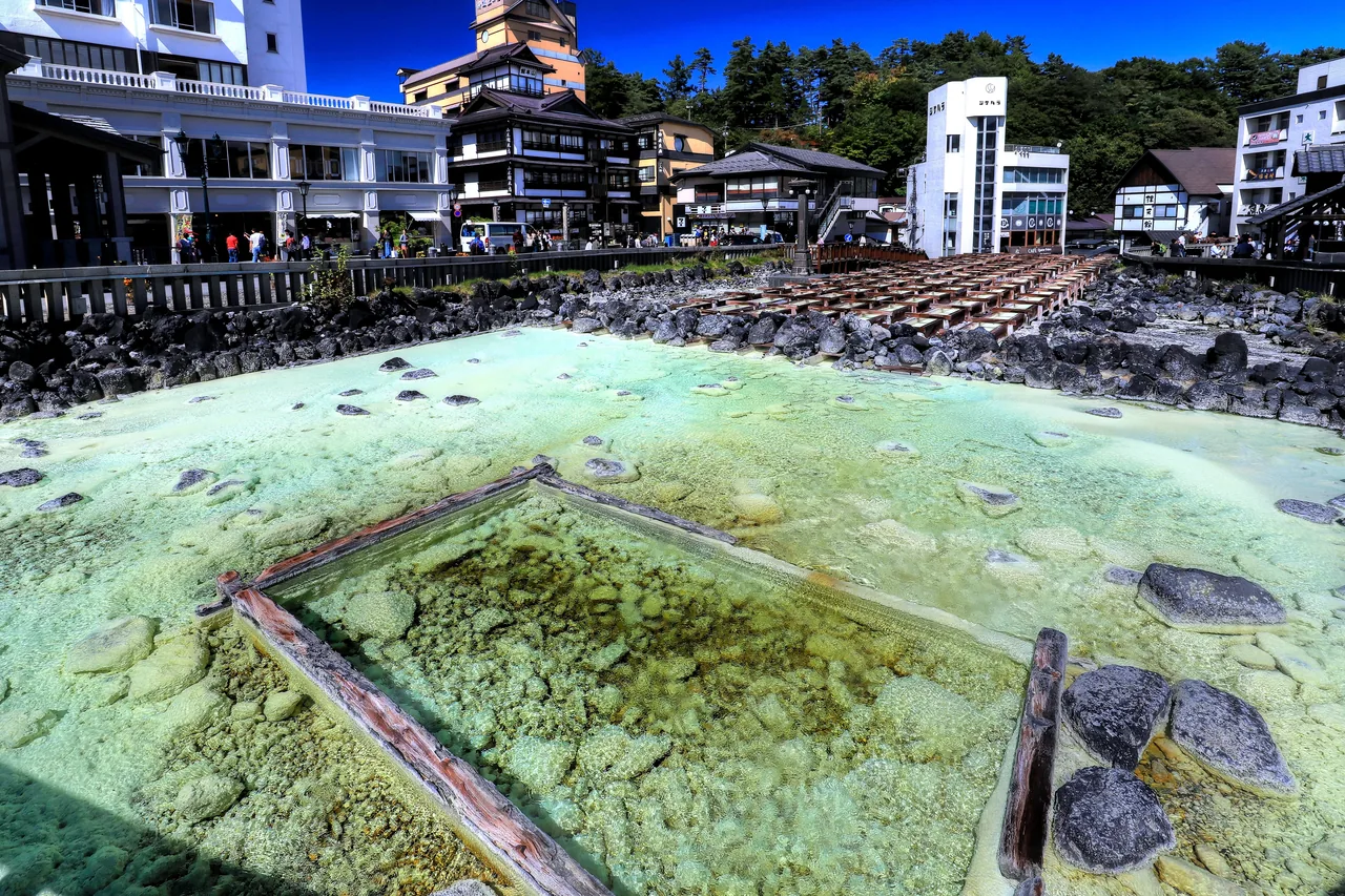 Hot spring water running through open wooden channels in the middle of a town, steam rising off the surface, with a railed walkway around it