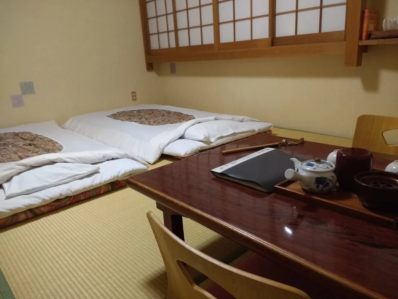 A tatami-matted guest room with a low table and flat floor cushions set out in the middle of the floor