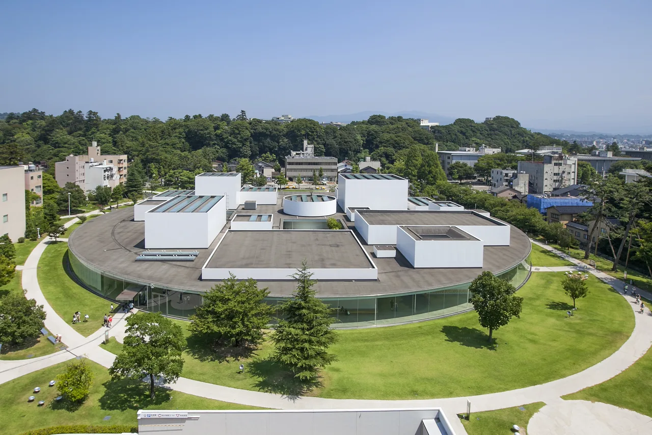 The circular white building of the 21st Century Museum seen from above, surrounded by lawn and paths