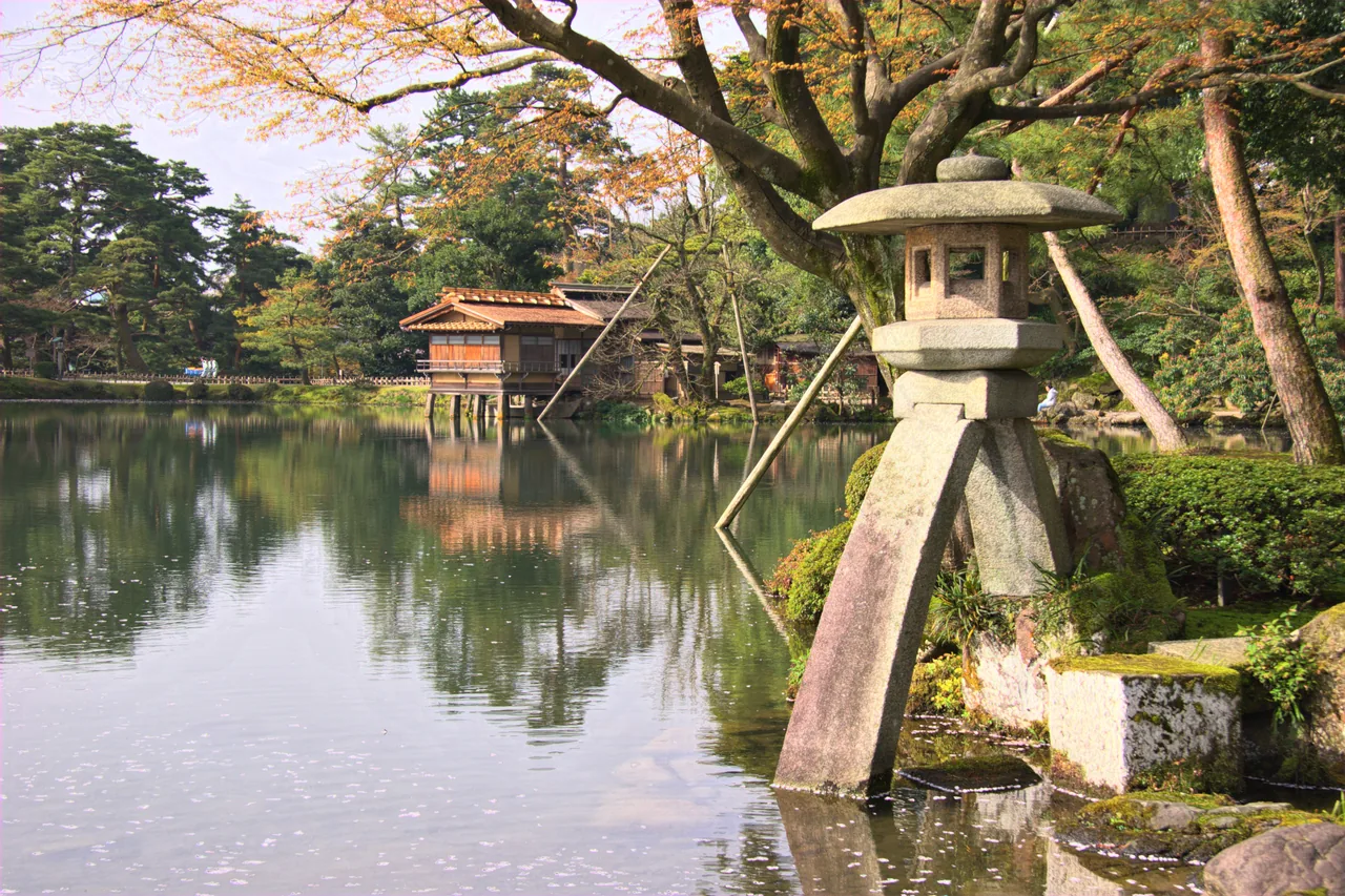 The stone Kotoji lantern standing at the edge of the pond in Kenrokuen garden in Kanazawa, with pine trees behind it