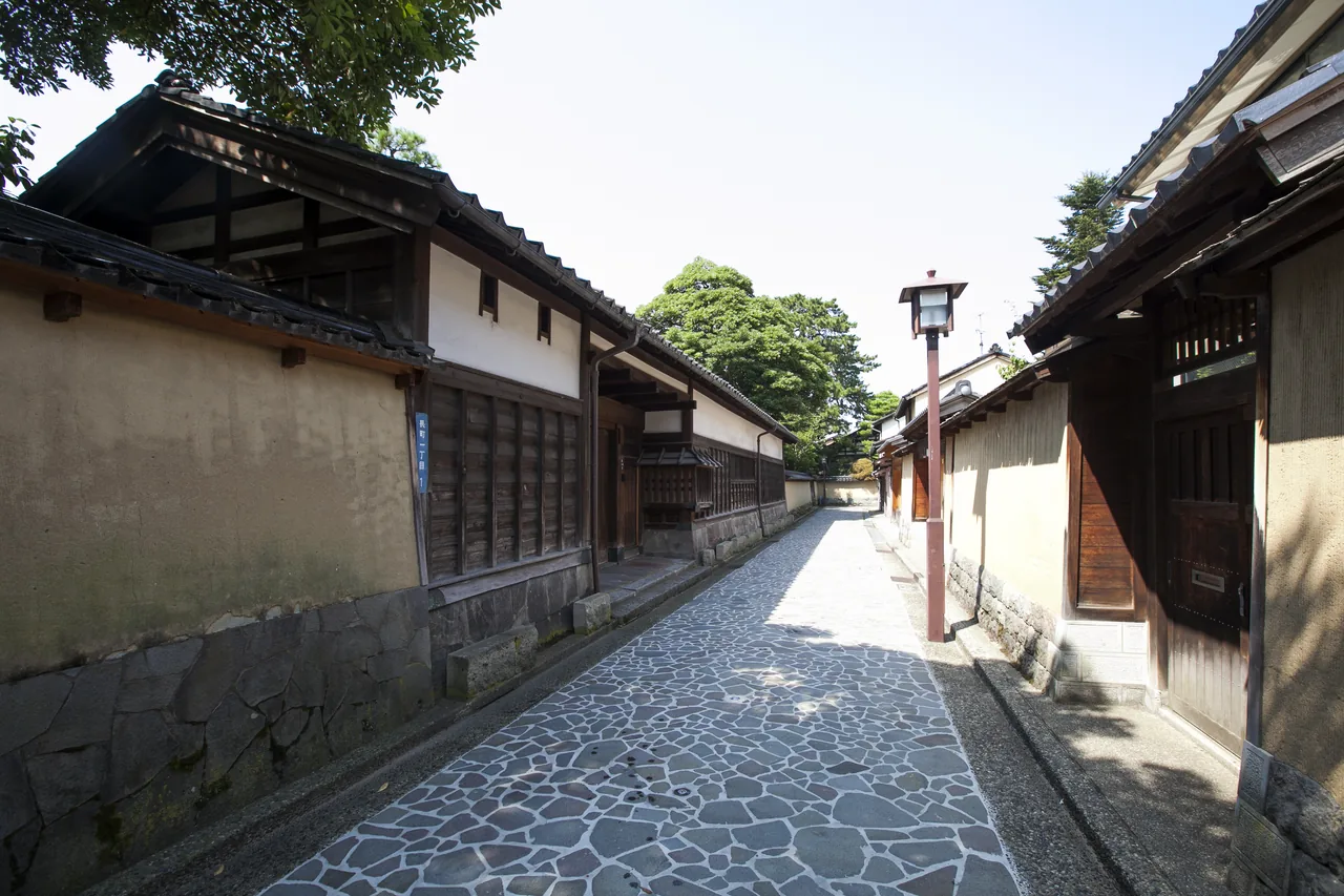 A narrow lane in Nagamachi between earthen walls with tiled tops, paved with fitted stones