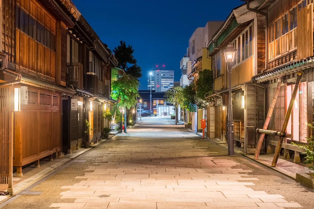 The Nishi Chaya District after dark, with lamps lit along the paved street and wooden facades on both sides