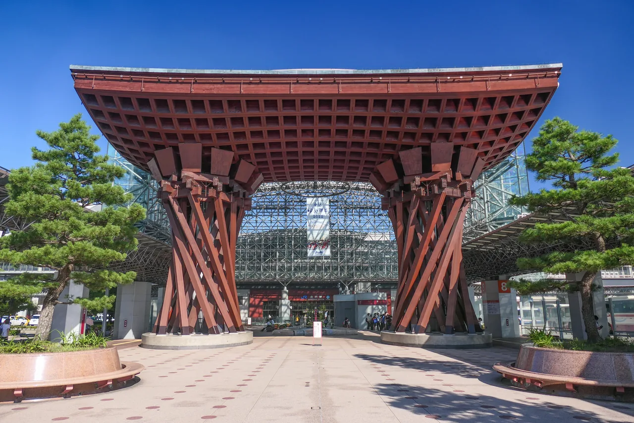 The Tsuzumi-mon gate outside Kanazawa Station, two timber columns under a curved roof, with a glass canopy behind