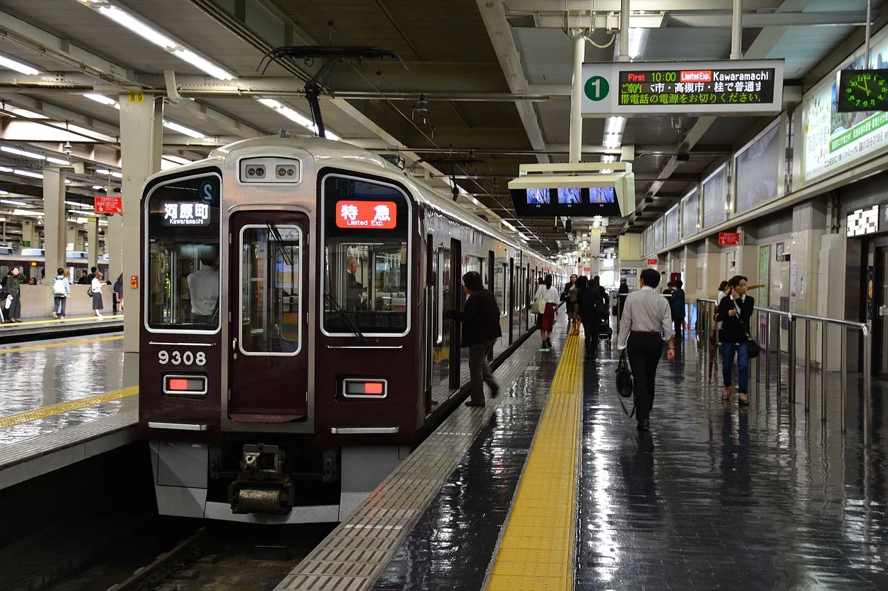 A Hankyu 9300 series train at an Osaka-Umeda platform with a limited express sign, passengers walking along the platform