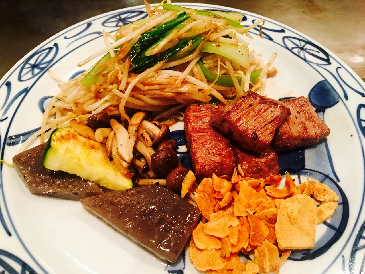 Slices of griddled beef on a patterned plate with bean sprouts, spring onion and vegetables alongside
