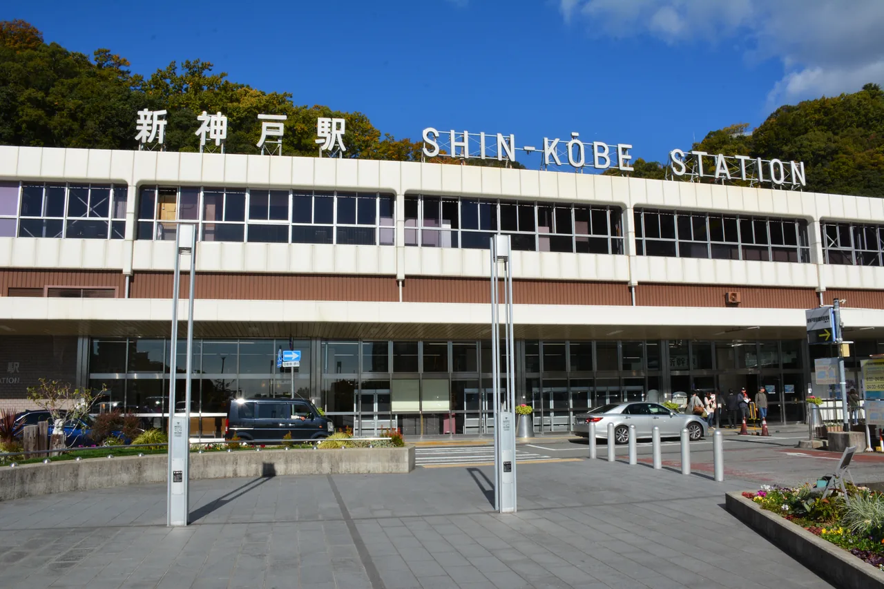 The exterior of Shin-Kobe station under a long sign reading Shin-Kobe Station, with the forecourt empty in front of it