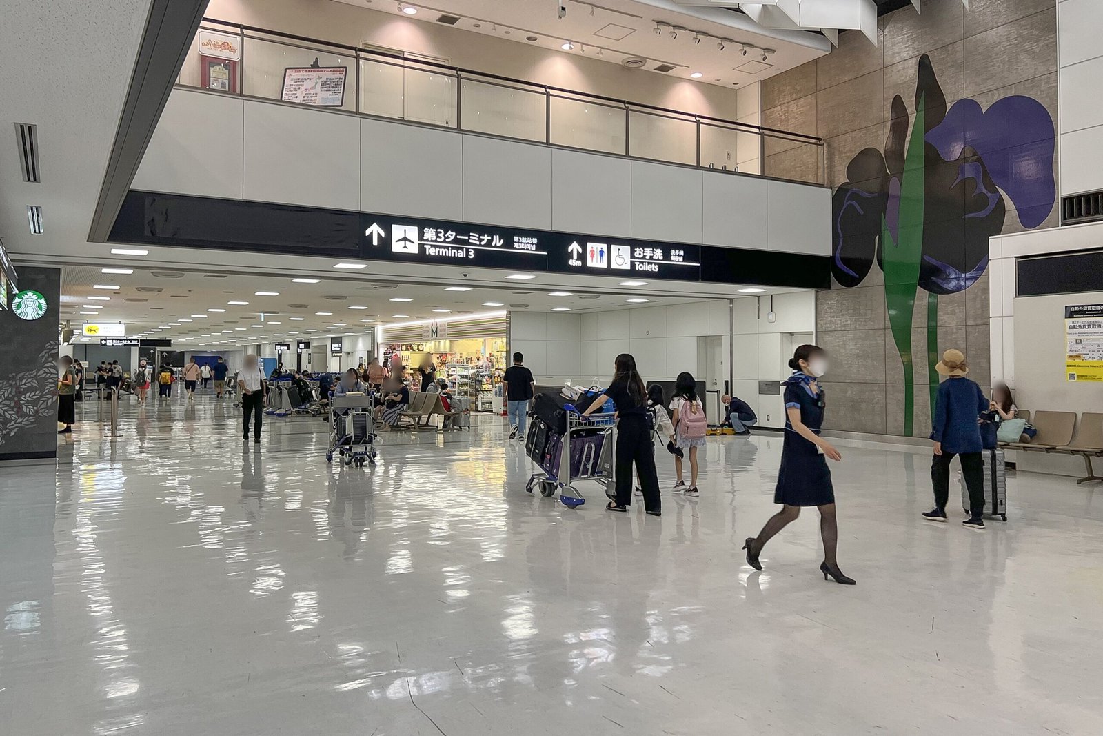 The arrival lobby of Narita Airport Terminal 2, with overhead signs to Terminal 3 and the toilets and travellers pushing baggage trolleys