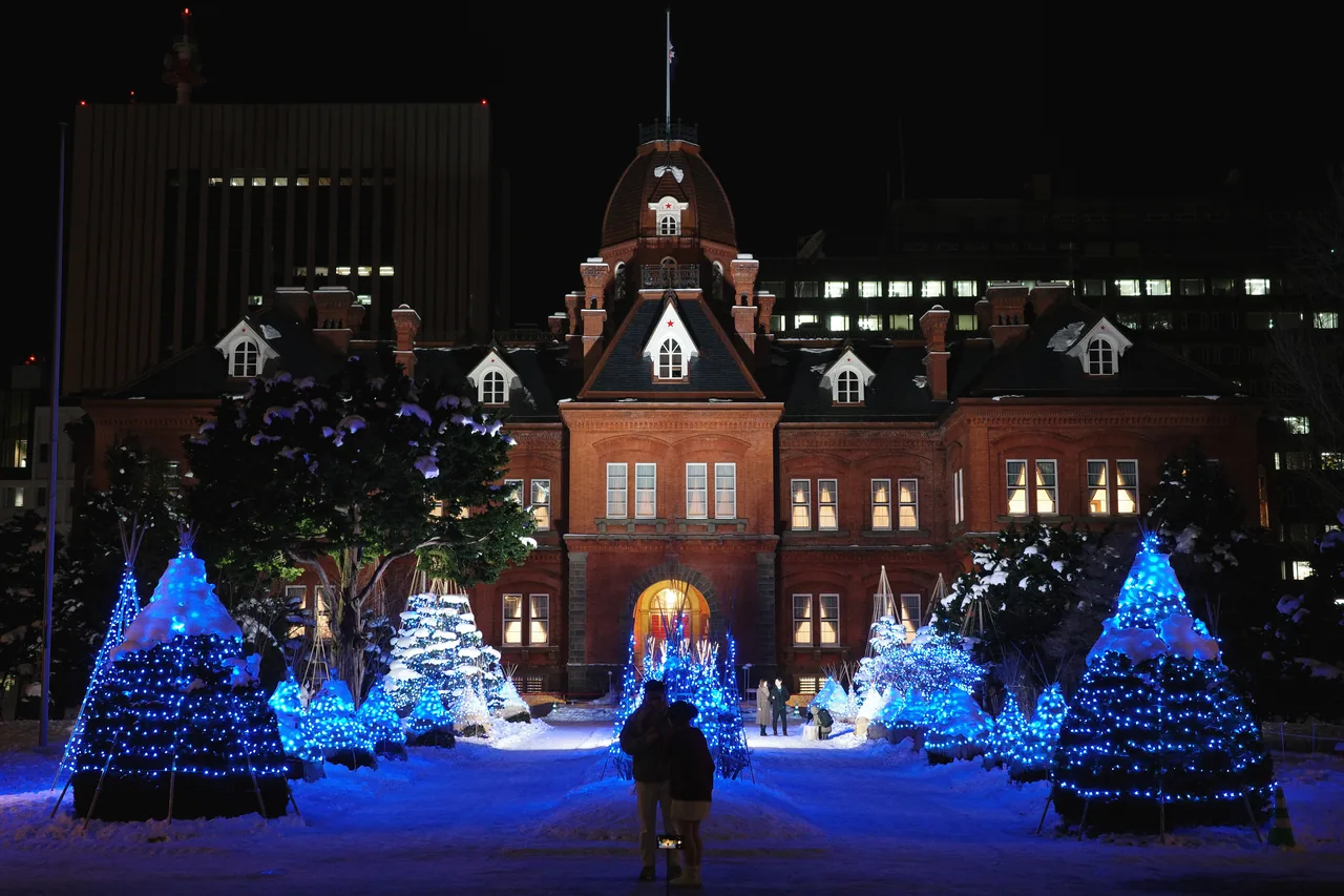 The red brick former Hokkaido Government Office lit at night, with blue illuminated trees in the snow