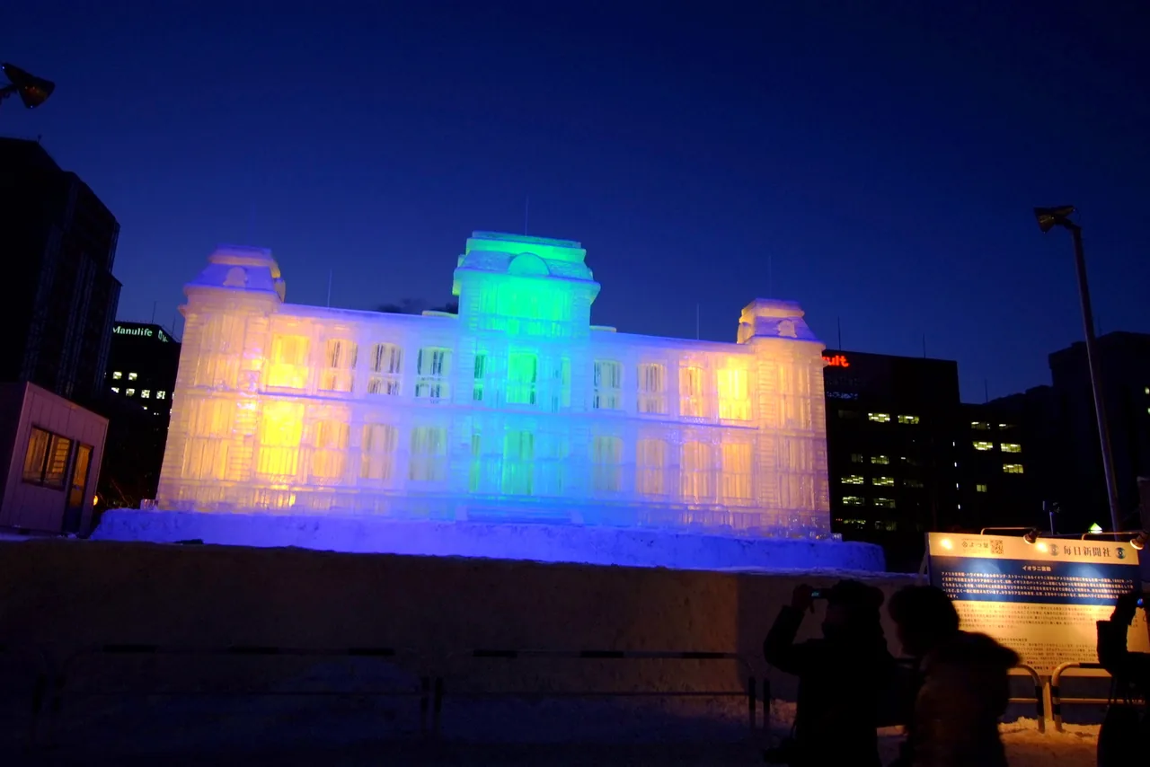 A large illuminated snow sculpture of a Western style building at the Sapporo Snow Festival at night