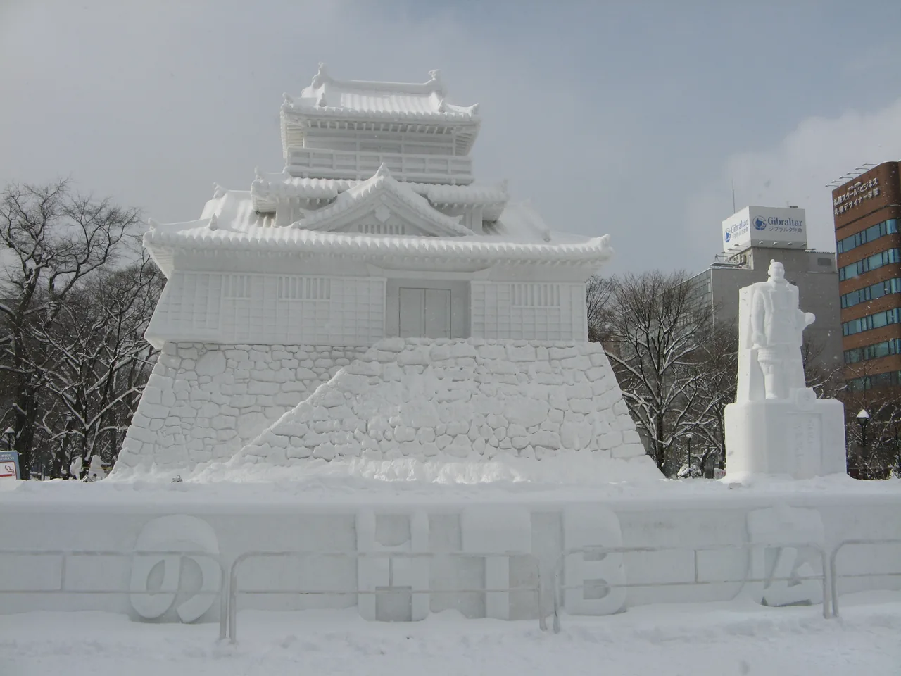 A large snow sculpture of a Japanese castle at Odori Park with office buildings behind it