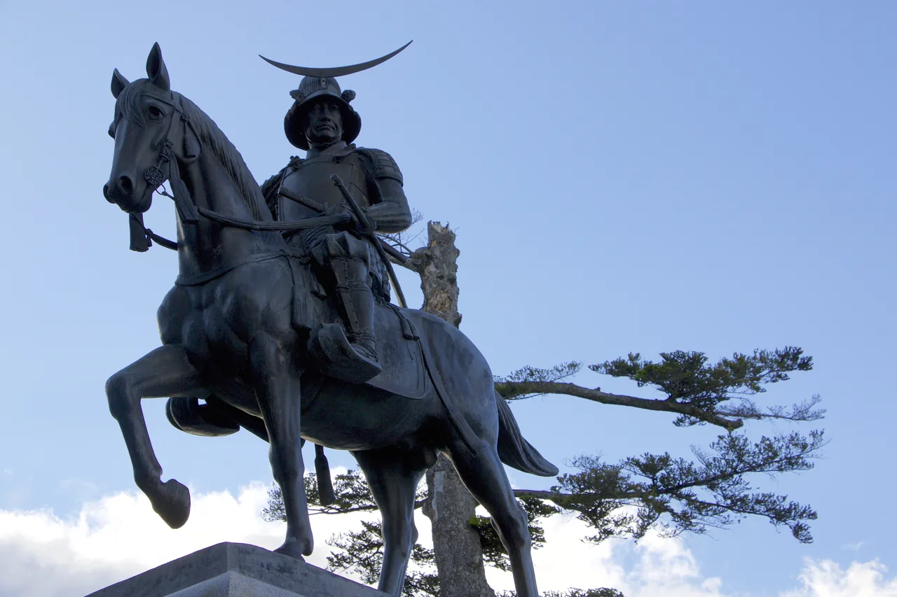The bronze equestrian statue of Date Masamune on the Sendai castle site, against a blue sky with a pine branch beside it