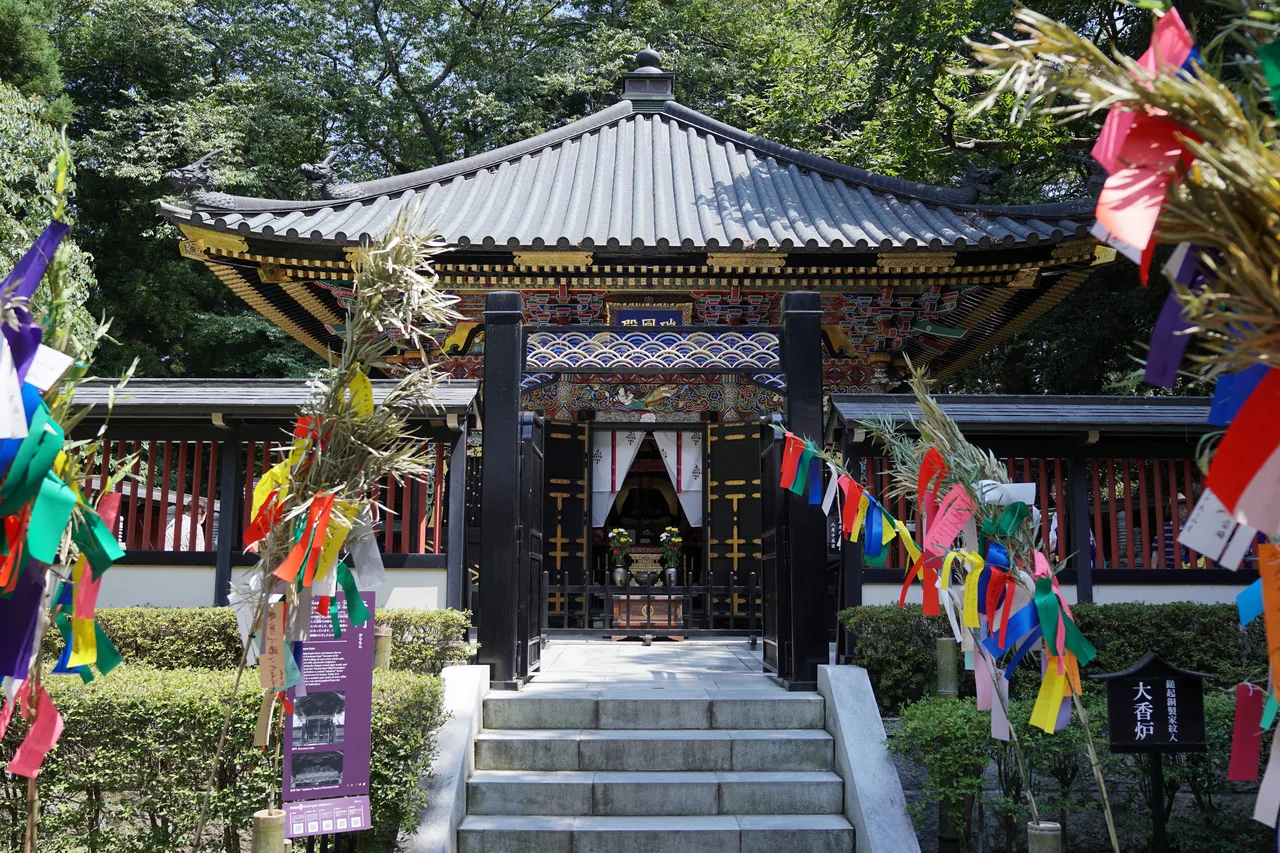 The Zuihoden mausoleum with painted carving and gold leaf across its facade, with festival streamers standing on either side
