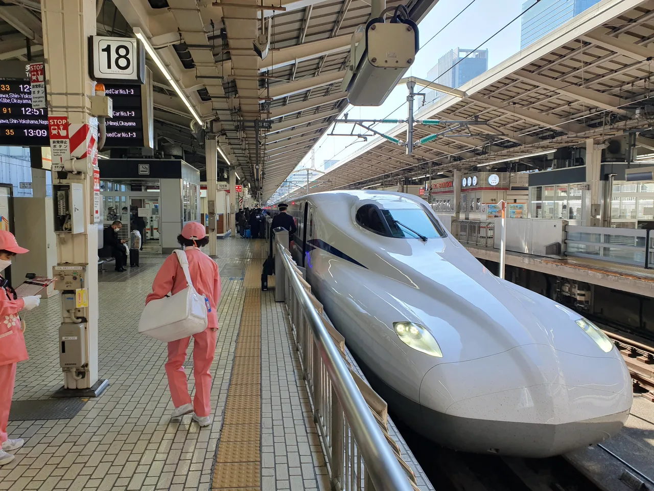 An N700S shinkansen at a Tokyo Station platform with travellers walking past carrying bags An N700S shinkansen at a Tokyo Station platform with travellers walking past carrying bags