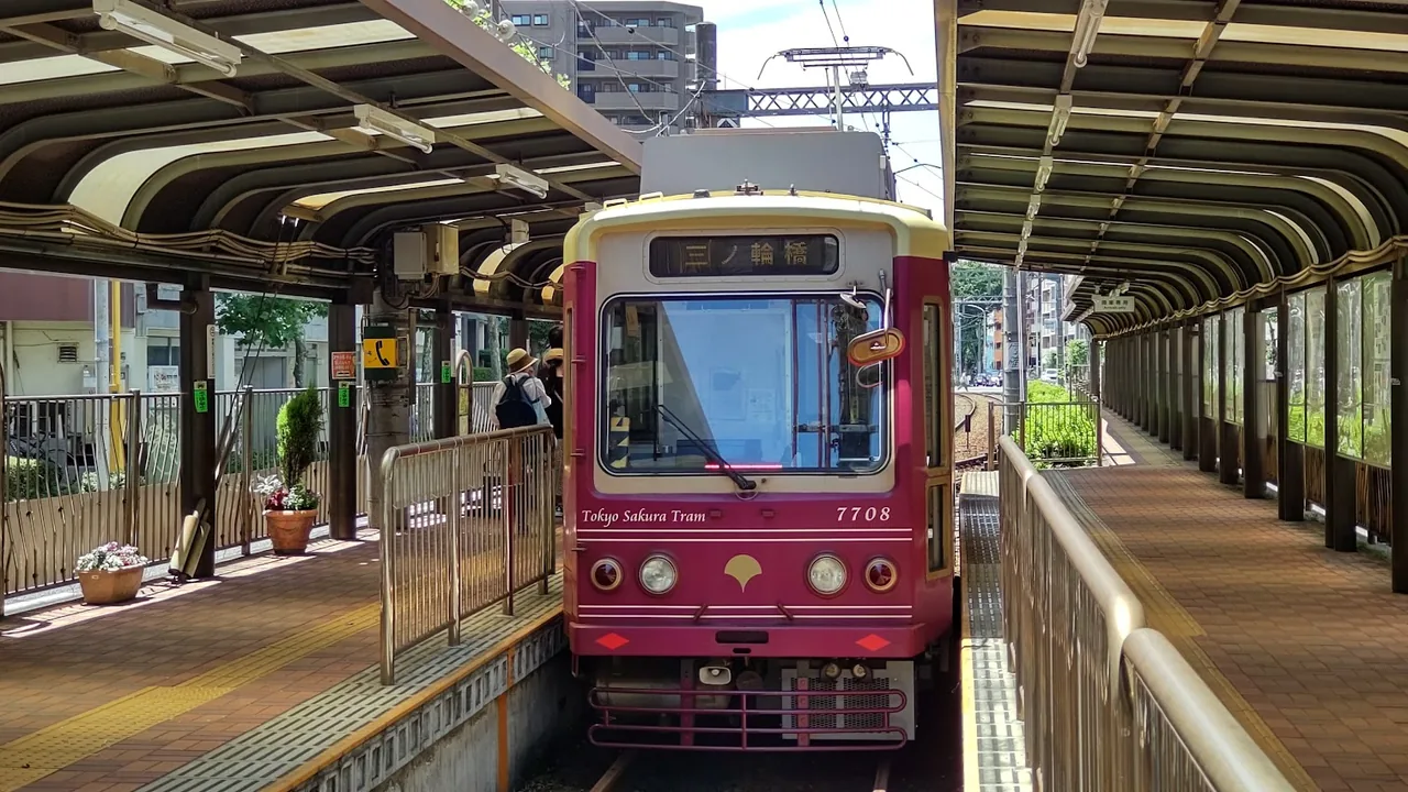 A Tokyo Sakura Tram car in rose and cream livery standing at a platform