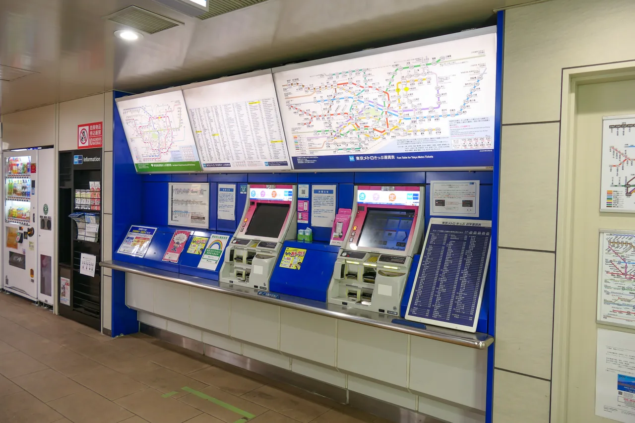 A row of ticket vending machines in a Tokyo subway station with a large fare map mounted on the wall above them