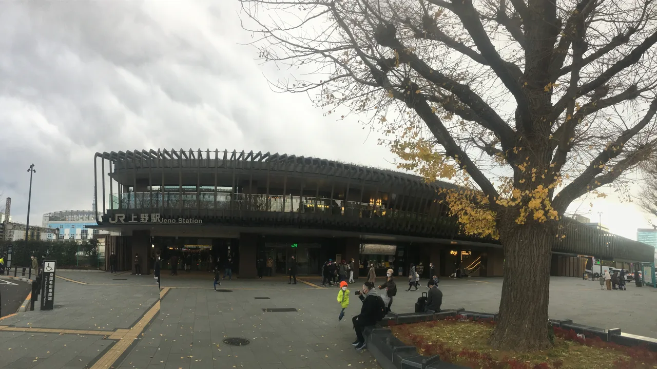 The Park Exit building of JR Ueno Station seen from the park side, with a large tree in front and people crossing towards it
