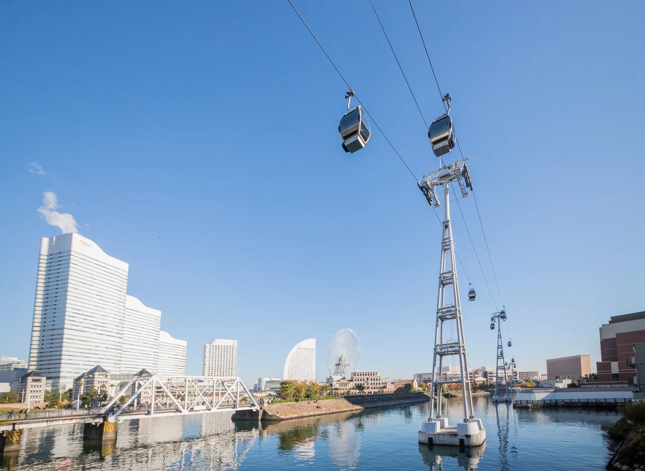 Cabins of the Yokohama Air Cabin ropeway crossing the canal on their cables, with Landmark Tower behind