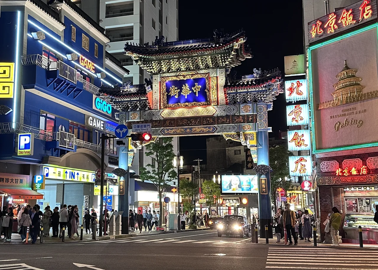 A decorated gate at the entrance to Yokohama Chinatown after dark, with lit shop signs down the street beyond