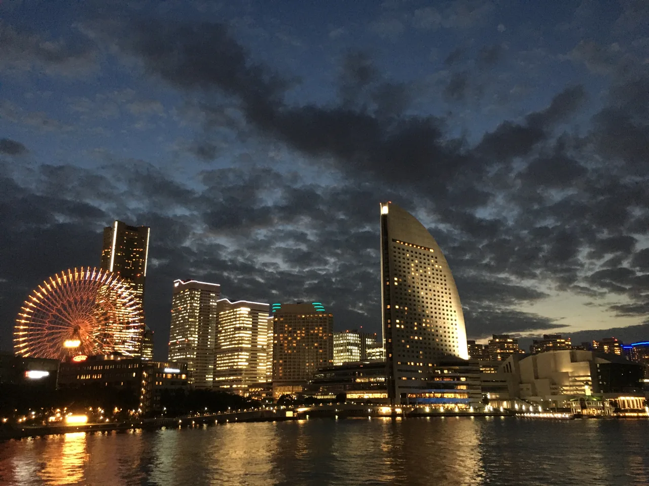 The Minato Mirai waterfront at dusk, with a lit ferris wheel on the left and the towers of the redevelopment standing along the water