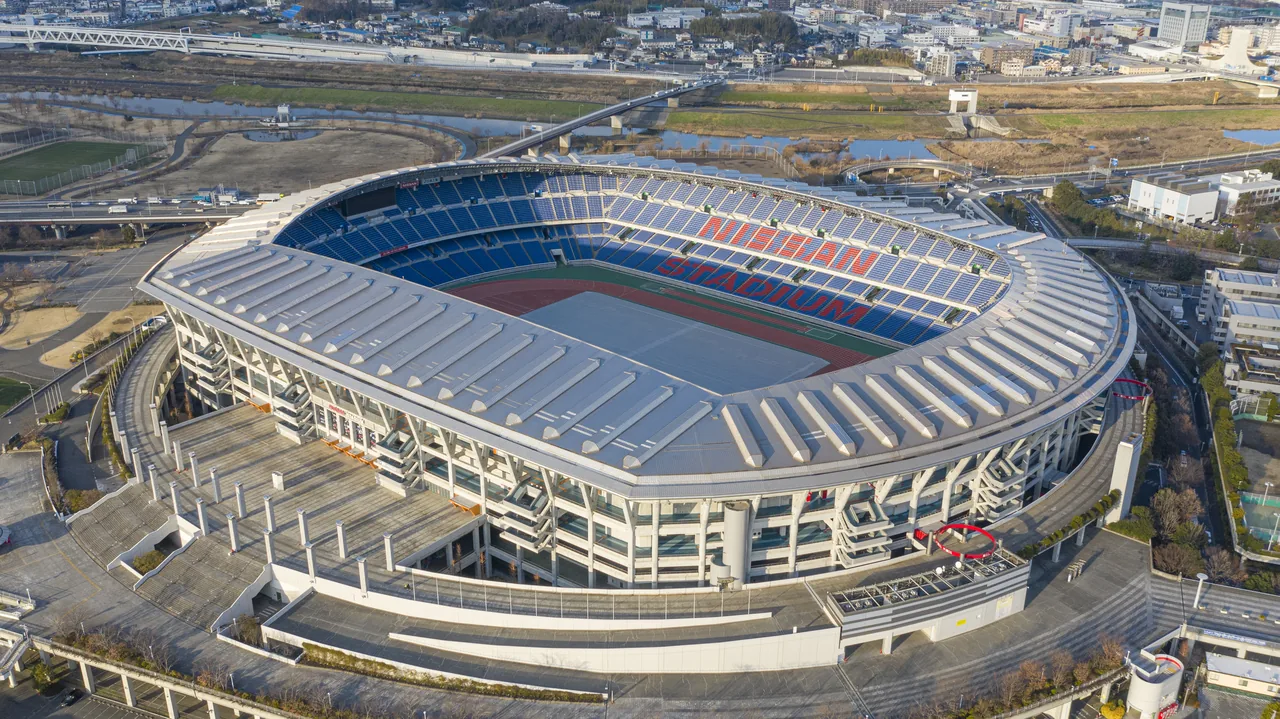 Nissan Stadium seen from the air, a large oval bowl ringed by a white roof, with the pitch and running track inside it