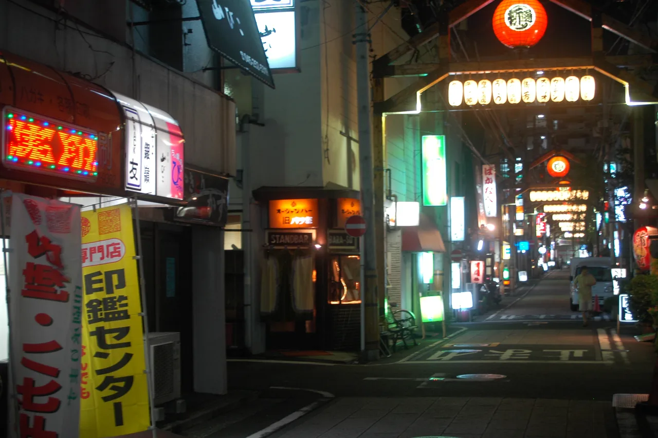 A narrow lane in the Noge district after dark, lined on both sides with small bars and eateries under lit signboards