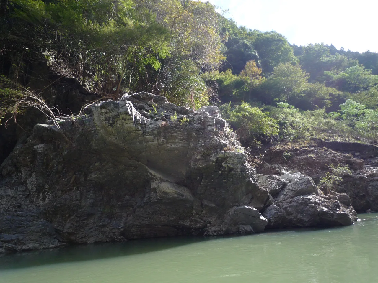 Rocks and clear shallow water in the Hozugawa gorge with forested slopes above