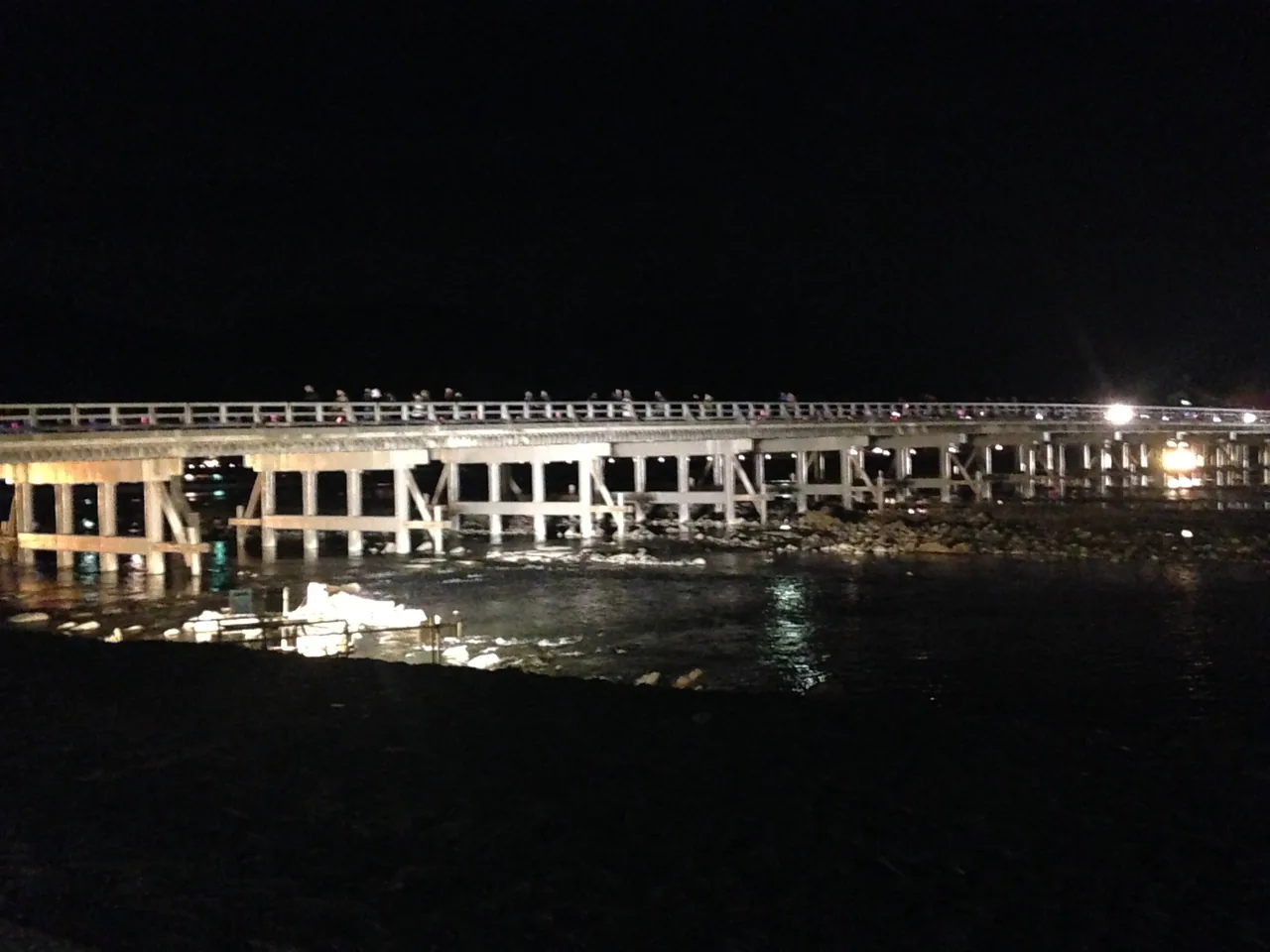 Togetsukyo Bridge lit at night with the dark mountain behind it