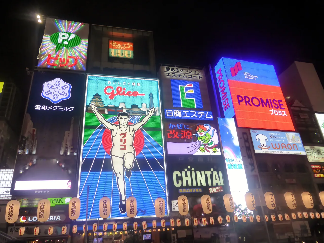 Lit neon and LED signs along the Dotonbori canal after dark, including the running man