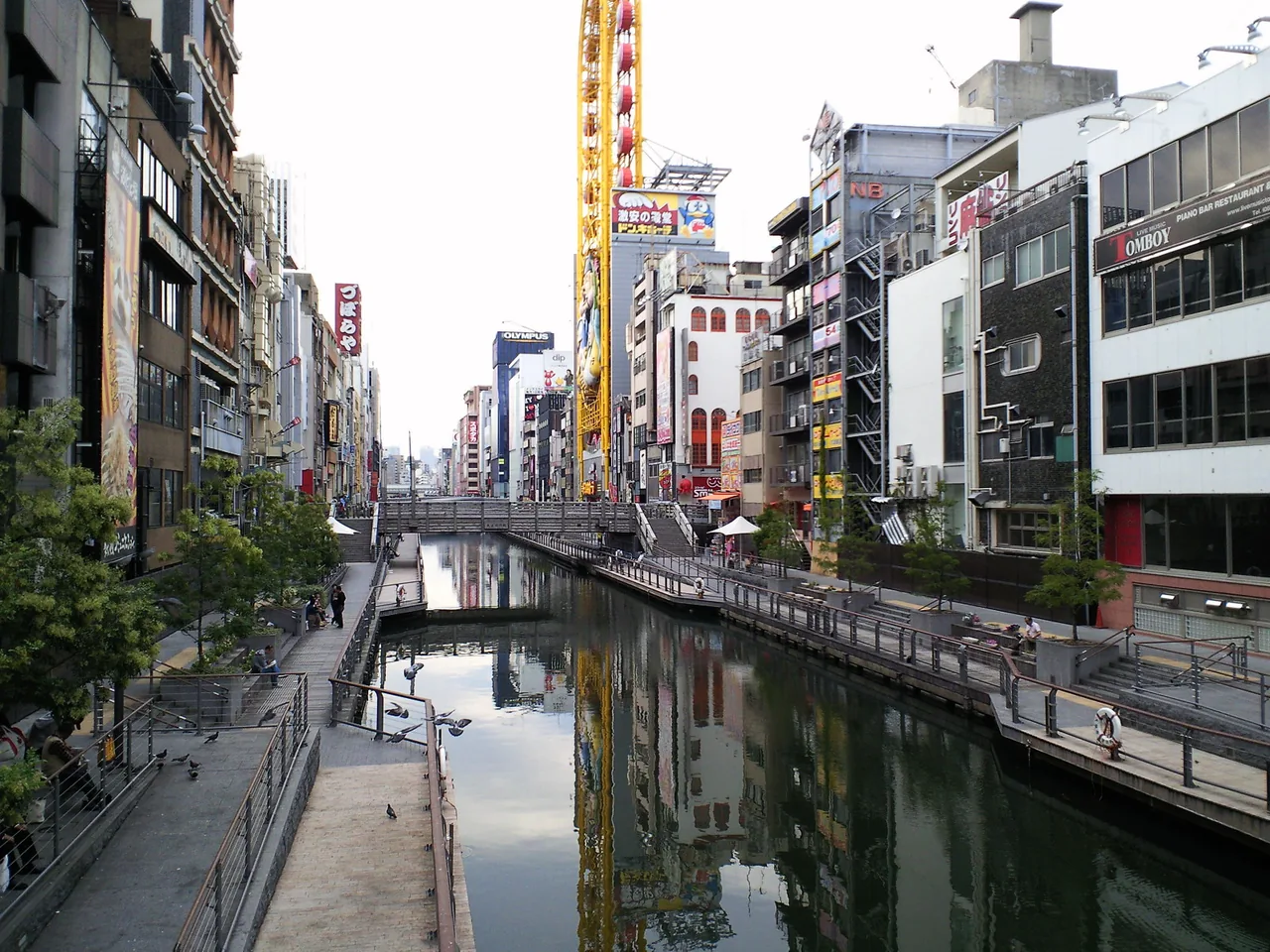 A paved walkway running along the water one level below the street in Dotonbori