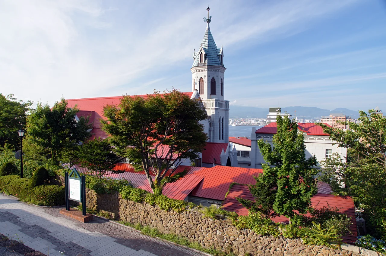 A church with a red roof and a tall tower on a slope above the town