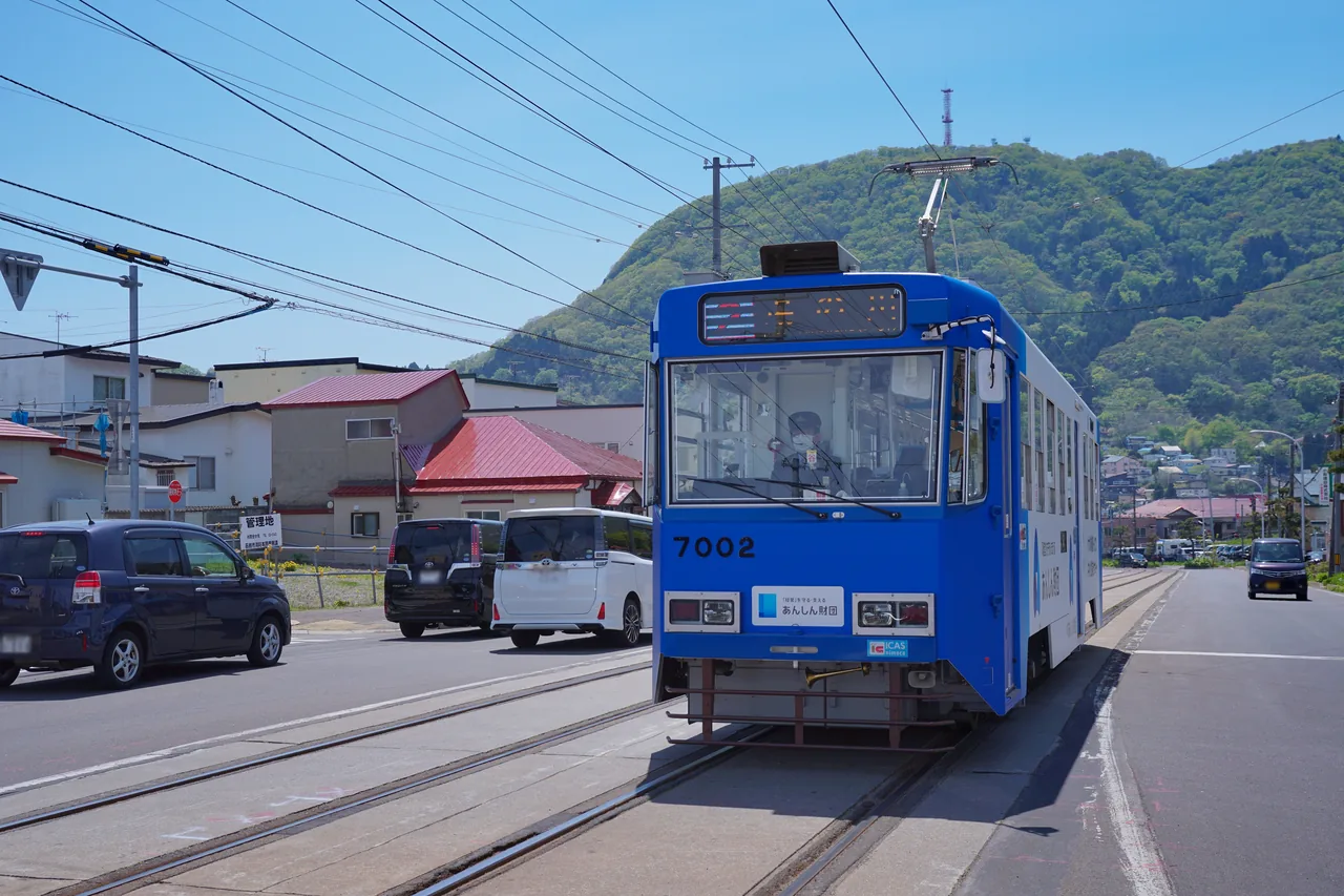 A blue and white tram on a city street with the mountain behind it