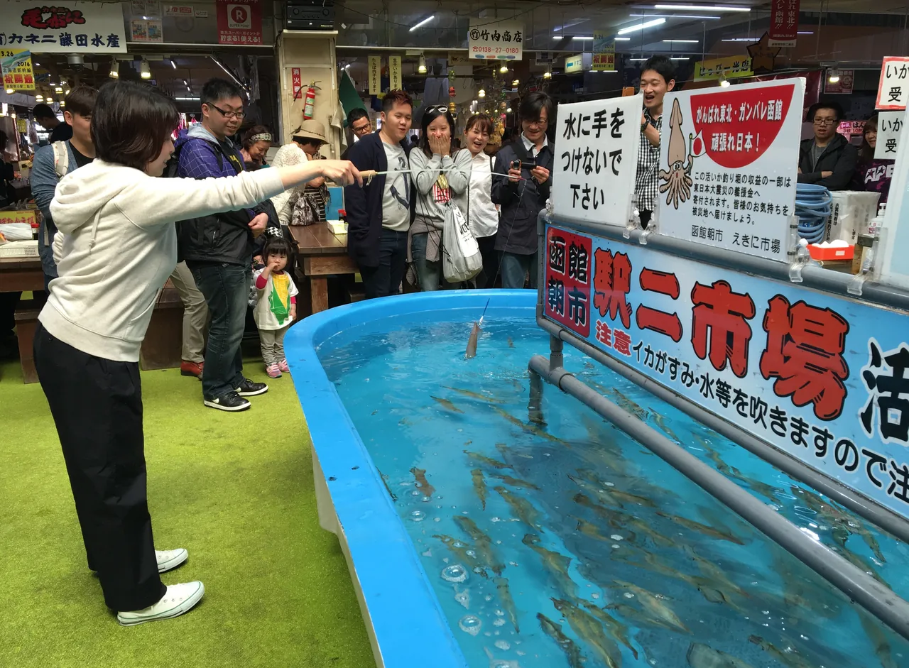 People leaning over a shallow tank in a market hall with rods in their hands
